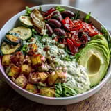 A hearty Vegan Mediterranean Buddha Bowl with mixed greens, chickpeas, avocado, and a drizzle of zesty tahini dressing.