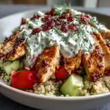 Freshly grilled lemon-herb chicken slices rest atop fluffy quinoa in this Greek Chicken Power Bowl, garnished with cherry tomatoes, cucumbers, and creamy tzatziki.