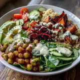 Colorful Buddha Bowl with Quinoa, Roasted Sweet Potatoes, and Crispy Chickpeas features avocado slices and red cabbage, drizzled with garlic tahini sauce.