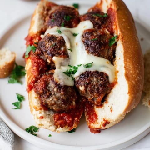 Warm photograph showing a delicious Meatball Sub with melted cheese and fresh, vibrant garnish herbs.
