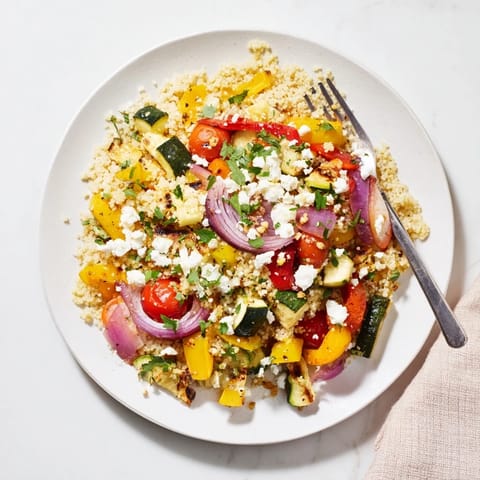 A colorful bowl of Roasted Veggie Couscous Salad with caramelized zucchini, peppers, and tomatoes tossed in bright lemon dressing.  