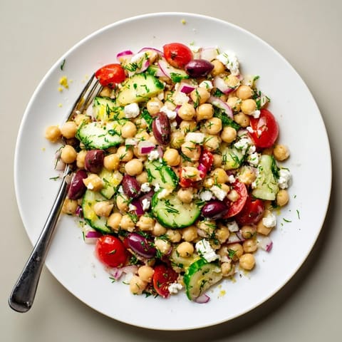 Lemon herb chickpea pasta salad served chilled in a white bowl, topped with crumbled feta and sliced kalamata olives for a Mediterranean twist.  