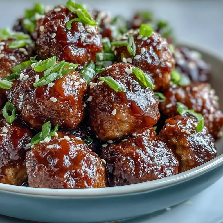 Tender frozen meatballs coated in a sweet and sour glaze garnished with green onions, served as a party appetizer.
