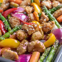 A close-up of tender Sheet Pan Honey Garlic Chicken and vibrant vegetables glistening with sweet-savory glaze, served hot.