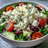 Fresh Greek Salad Bowl topped with crumbled feta, Kalamata olives, and diced tomatoes on crisp romaine, drizzled with oregano vinaigrette.