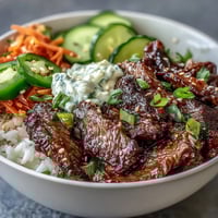 Fluffy white rice and sesame-ginger marinated beef create the base of this Korean Beef Power Bowl, garnished with pickled carrots, cucumber, and fresh jalapeños.