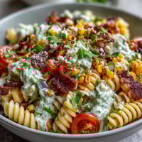Vibrant Elote Pasta Salad with Cotija, Chili and Lime, featuring charred corn, creamy cheese, and zesty dressing in a colorful bowl.