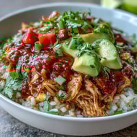 Vibrant salsa chicken bowls with shredded chicken, rice, black beans, and fresh avocado, topped with cilantro and lime.